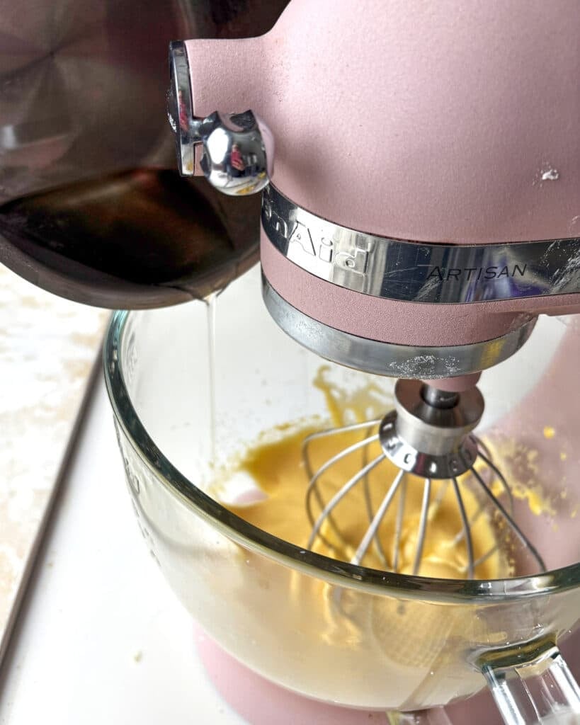 Pouring hot sugar syrup into whipping egg yolks to make French buttercream. 