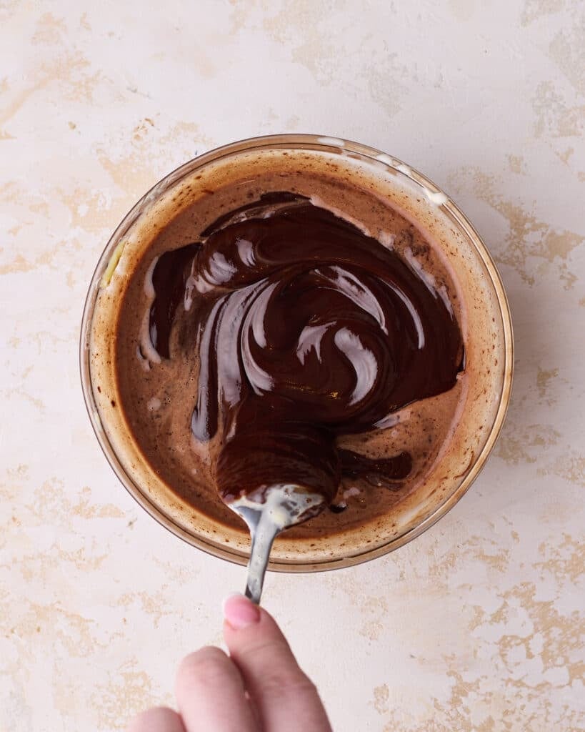 Mixing shiny chocolate glaze in a glass bowl to go on top of opera cake. 