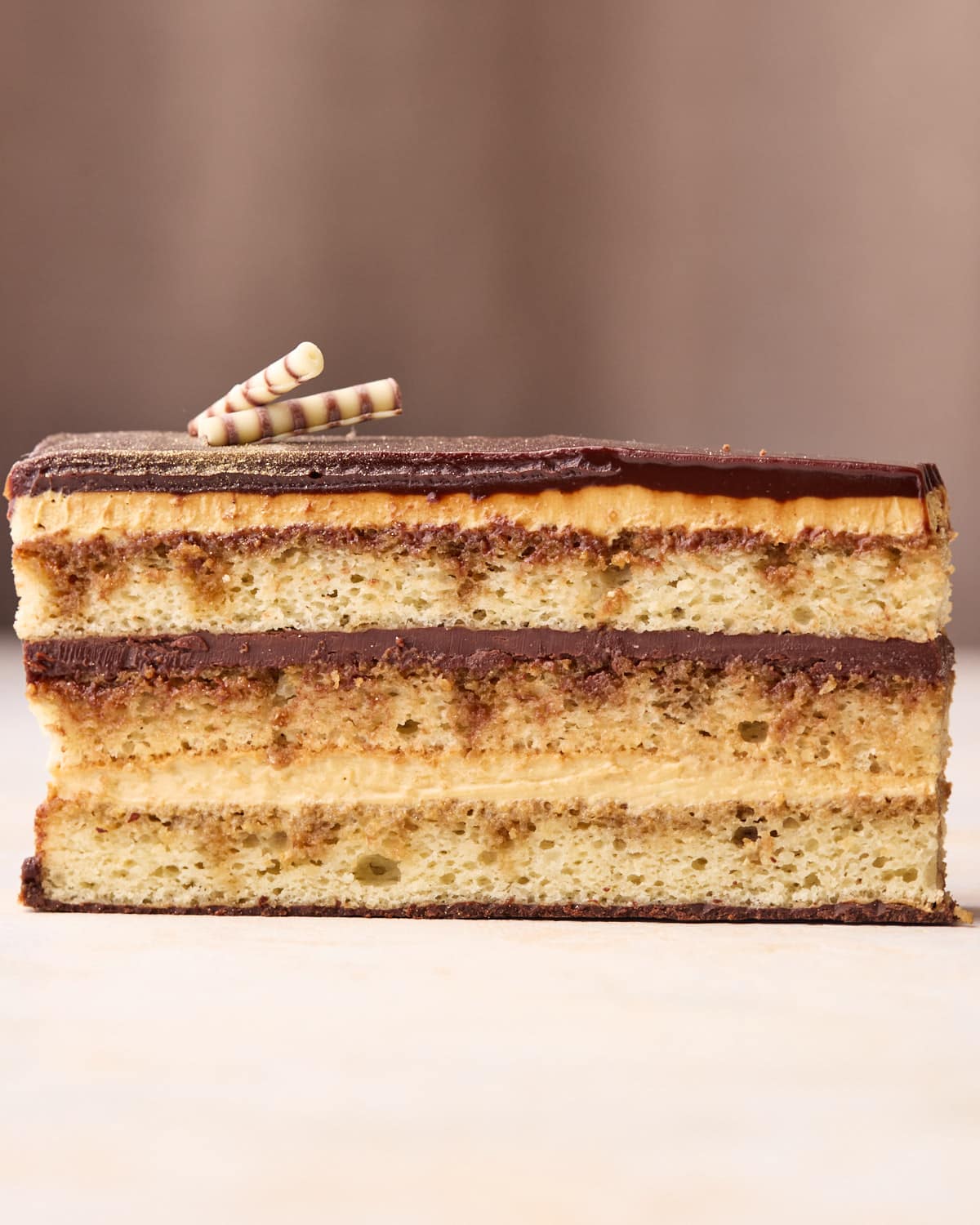 Single slice of opera cake showing the layers of joconde, french buttercream, and chocolate ganache. 