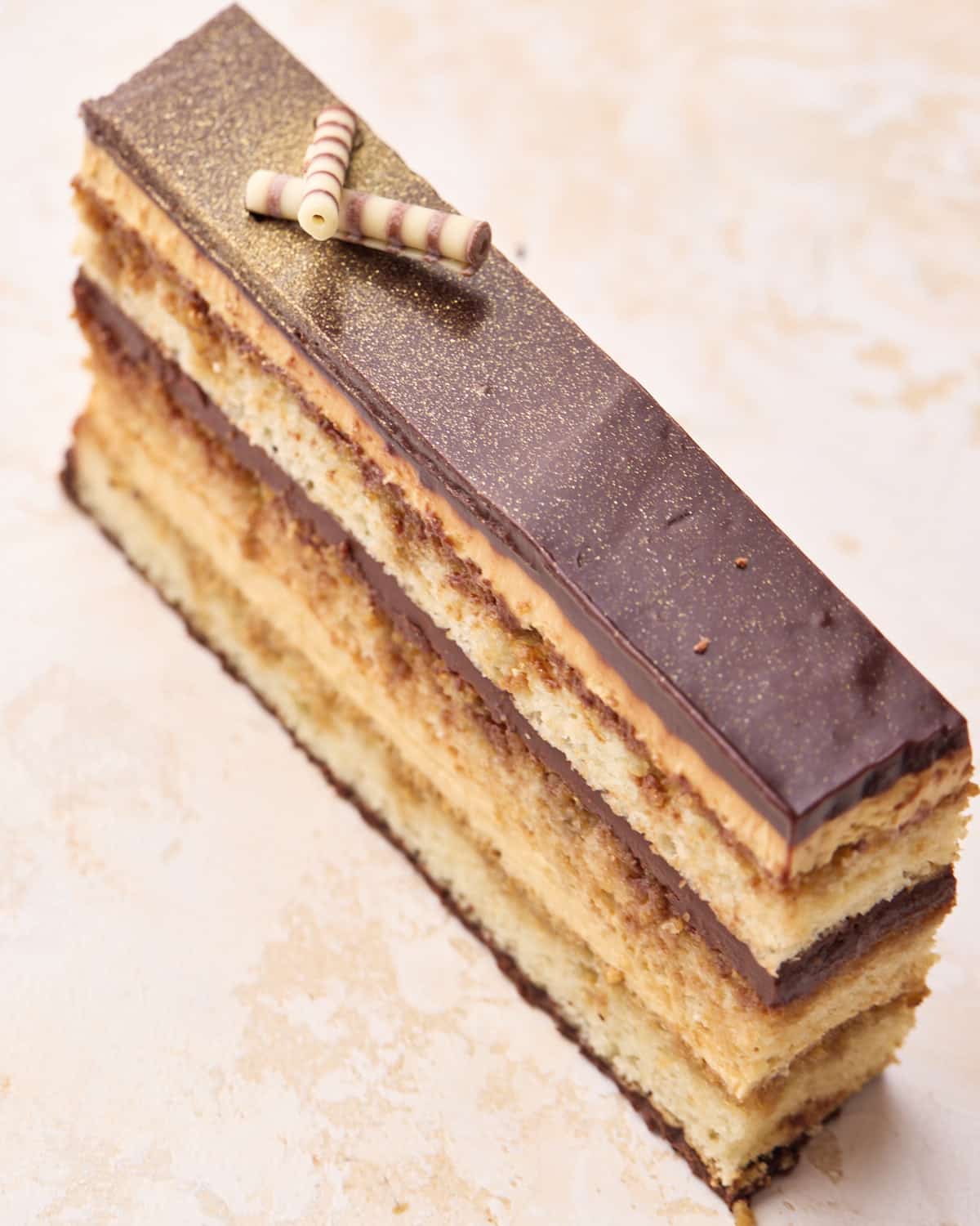 Slice of opera cake showing the shiny chocolate ganache and seven layers inside. 