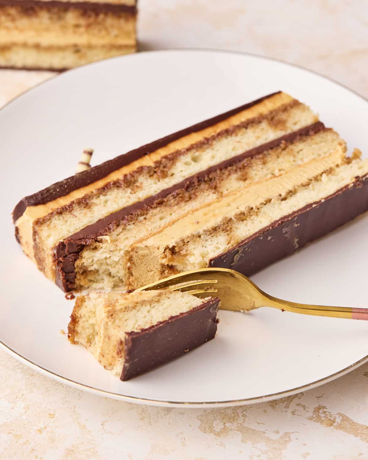 Slice of opera cake on a plate with a bite being taken out. 