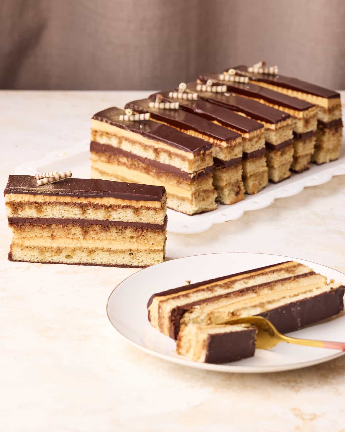 Several slices of opera cake on a serving plate, one is laying down on a plate with a bite taken out of it. 