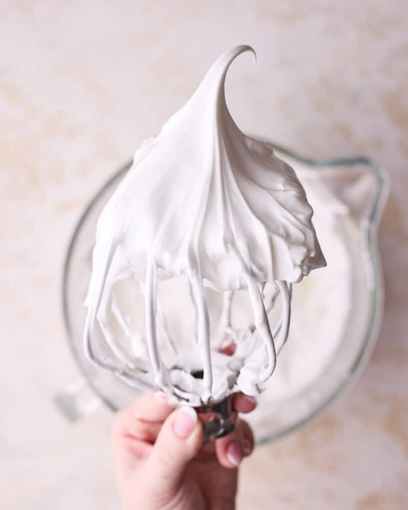 Meringue on a stand mixer whisk showing firm peaks. 