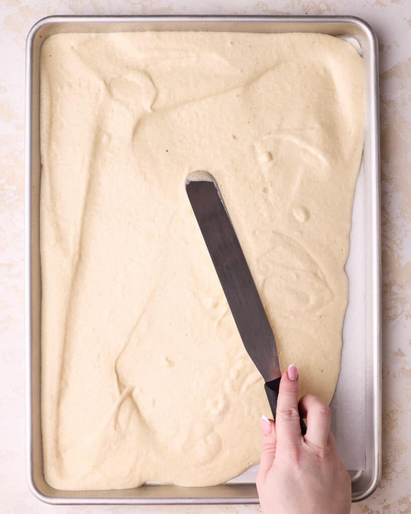 Smoothing joconde sponge batter with a straight spatula in a sheet pan to make a layer of joconde sponge for Opera cake. 