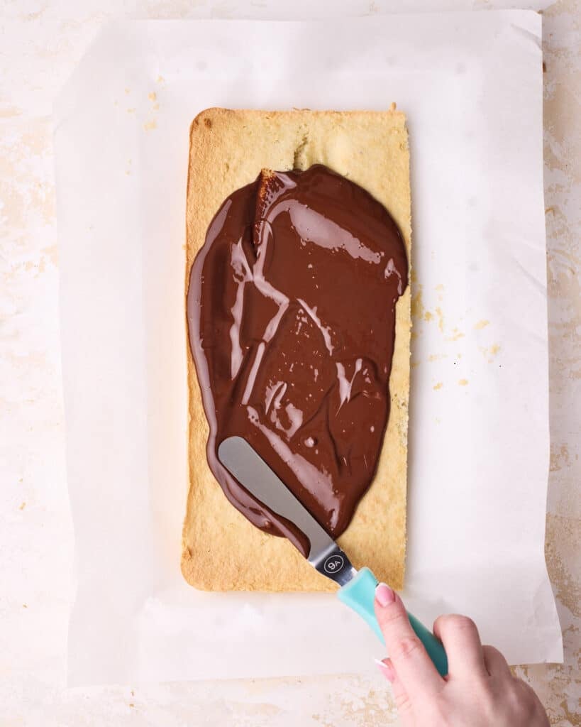 Spreading melted chocolate onto a rectangle of joconde sponge to make the base layer of Opera cake. 