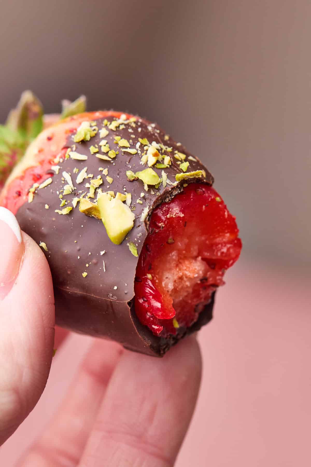 Chocolate covered strawberry with pistachios on top, with a bite taken out of it. 