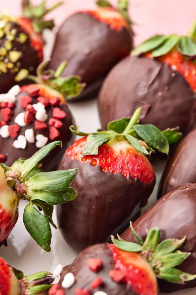 Chocolate covered strawberries on a tray with various toppings.