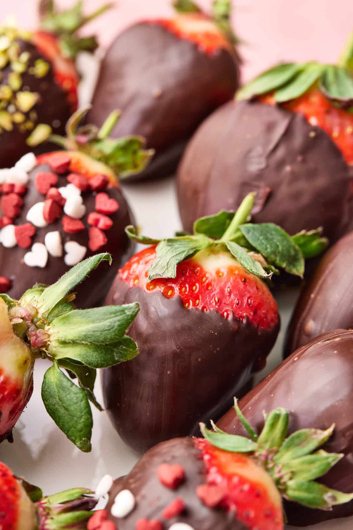 Chocolate covered strawberries on a tray with various toppings.