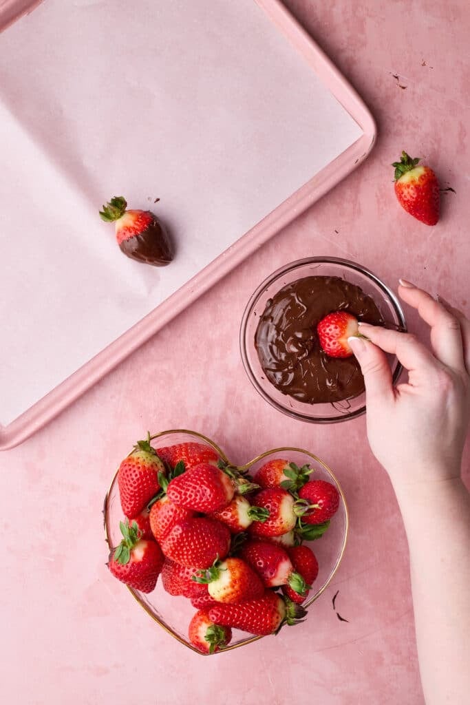 Dipping fresh strawberries in melted chocolate to make homemade chocolate covered strawberries. 