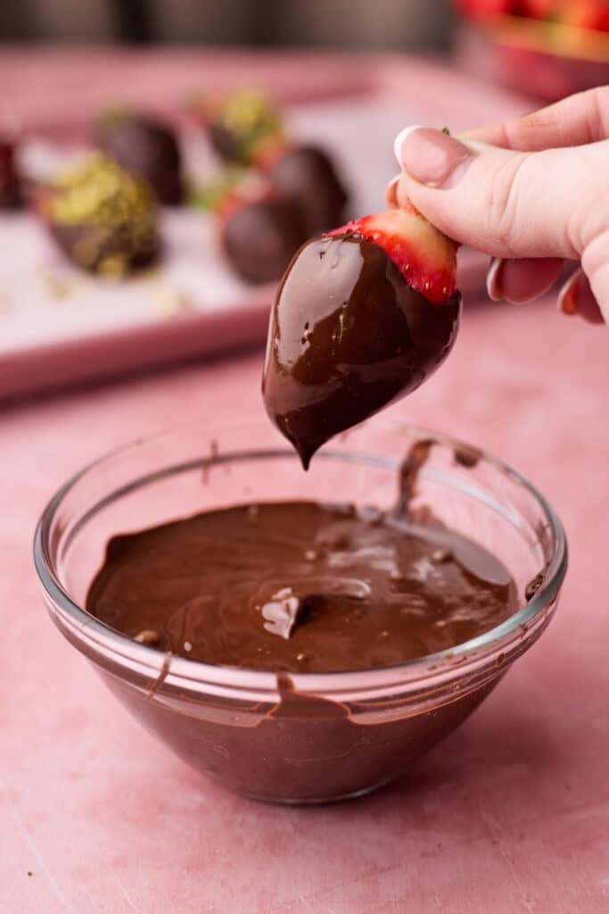 Shaking excess chocolate off of a strawberry. 