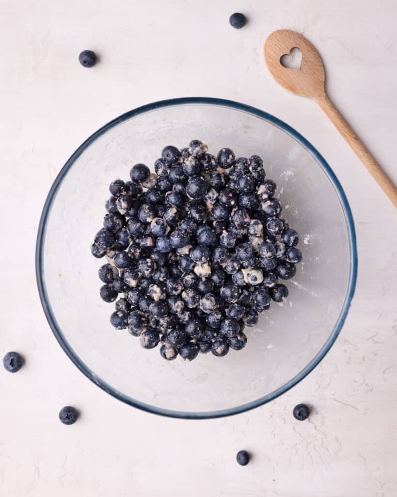 Fresh blueberries being tossed with flour, sugar and lemon juice in a glass bowl to make blueberry crumble. 