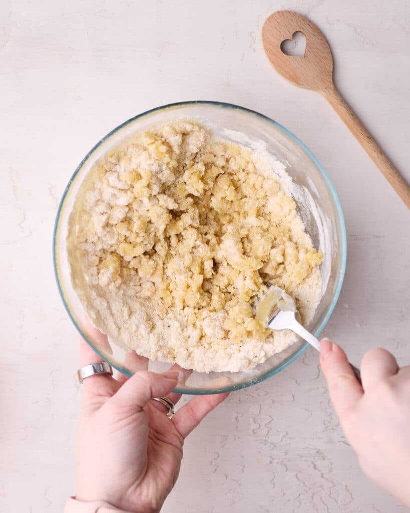 Crumble topping in a glass bowl being stirred with a fork.
