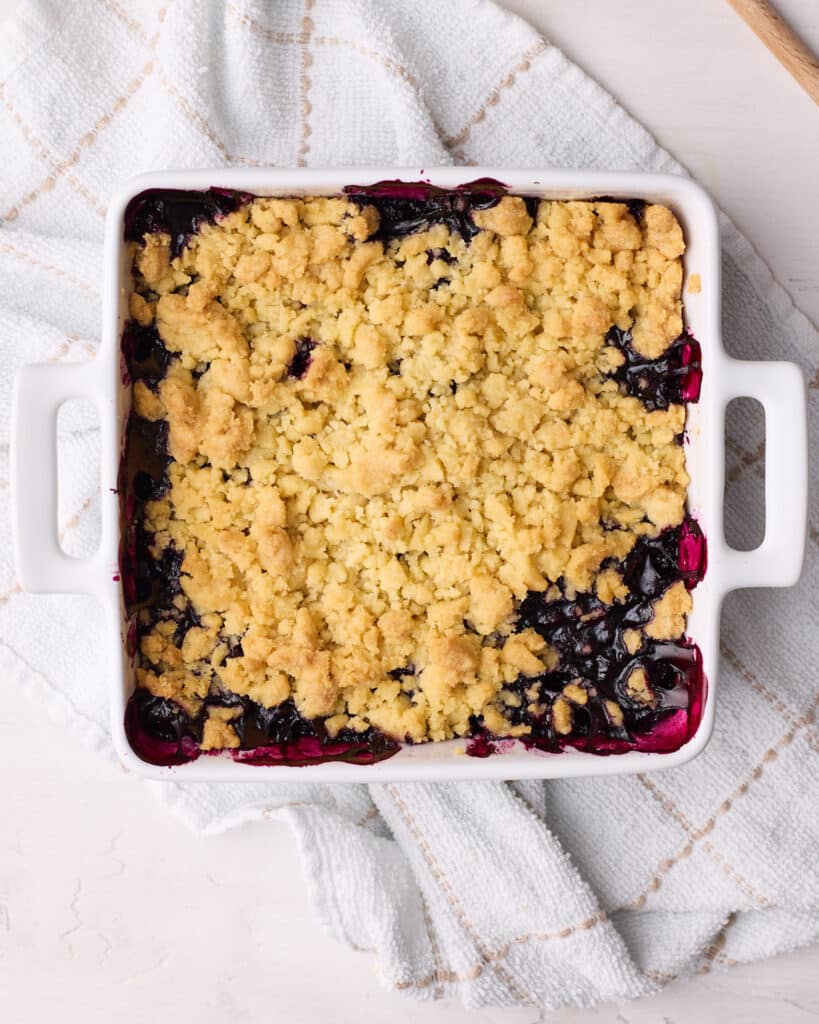 Baked blueberry crumble out of the oven, showing the blueberry juices bursting through the crumble. 