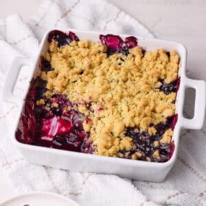 Homemade blueberry crumble in a baking dish with a portion scooped out of it to show the blueberry filling inside.