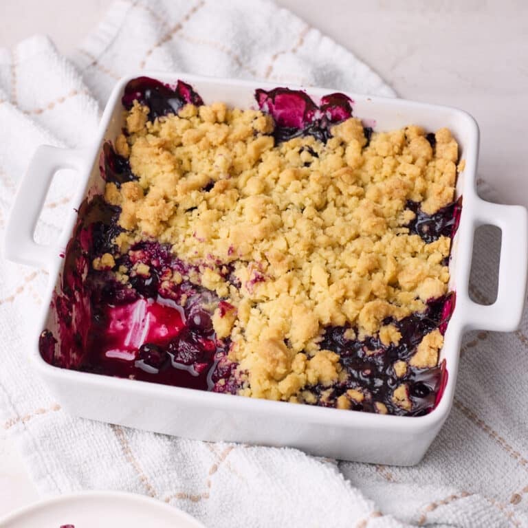 Homemade blueberry crumble in a baking dish with a portion scooped out of it to show the blueberry filling inside.