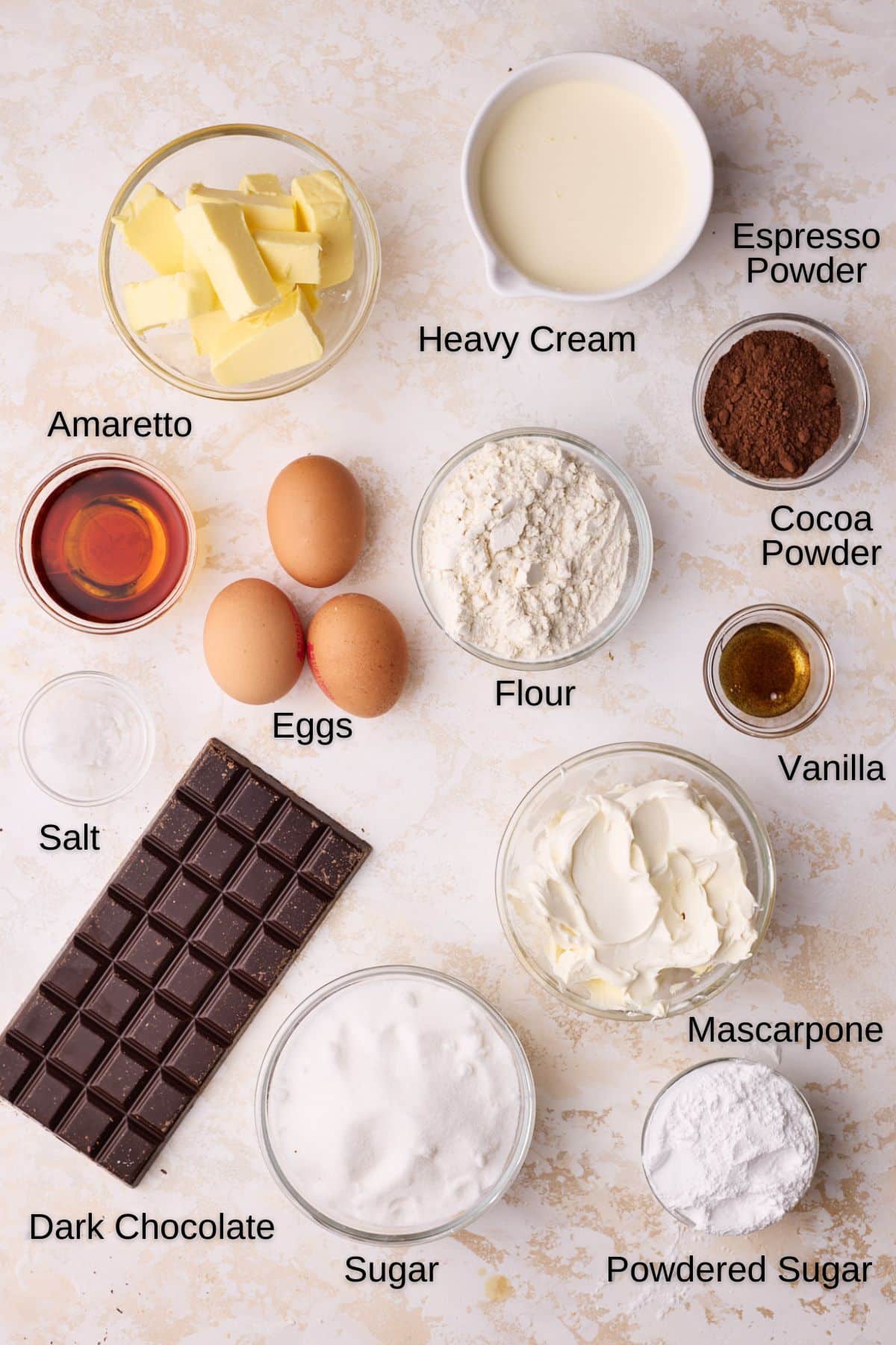 Ingredients to make Tiramisu Brownies, including butter, sugar, eggs, flour, dark chocolate, espresso powder, mascarpone cheese, heavy cream, powdered sugar, vanilla extract and amaretto. 
