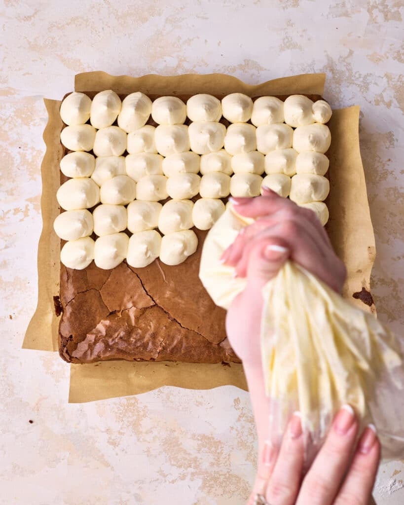 Piping mascarpone cream on top of espresso brownies to make Tiramisu brownies. 