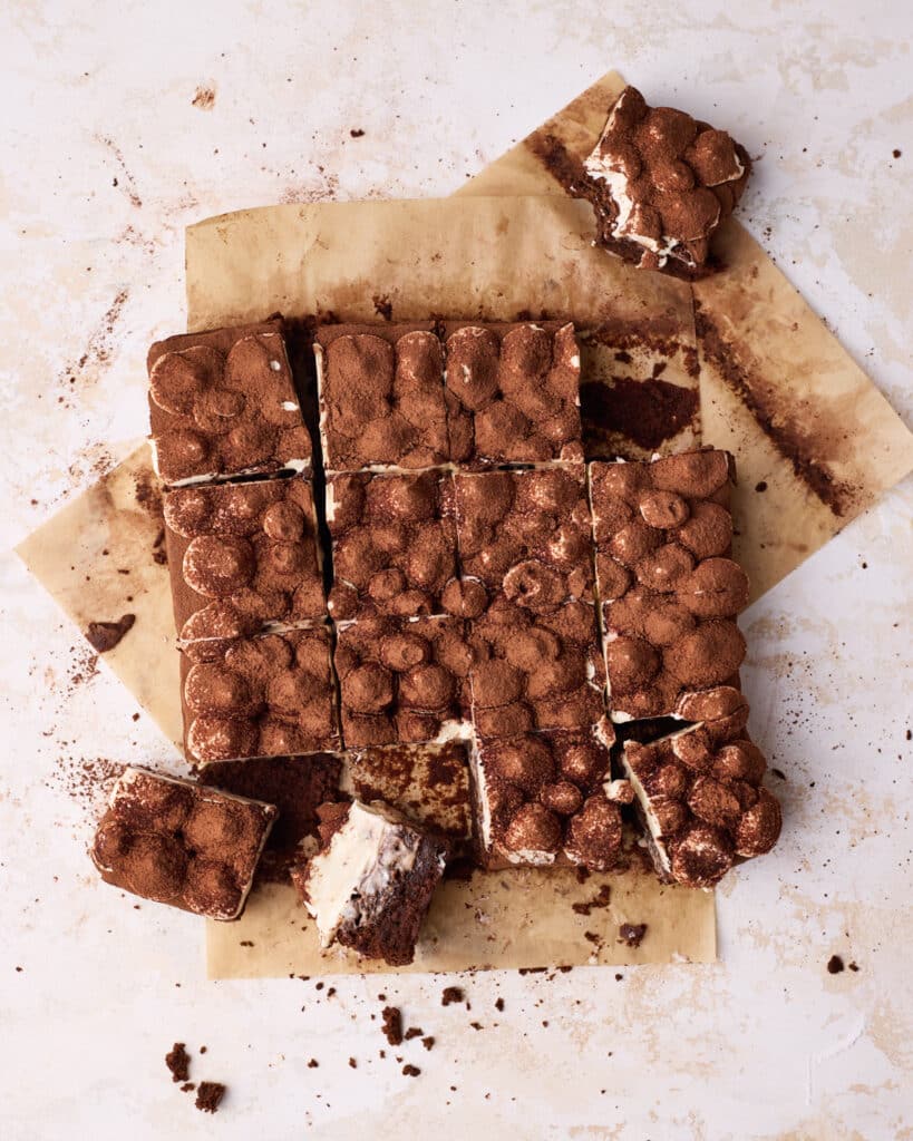 Tiramisu brownies on parchment paper sliced into 16 even squares. 