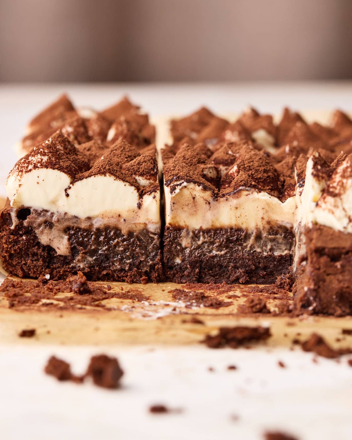 Tiramisu brownies on parchment paper after being sliced - a few pieces have been taken out to show the gooey centers.