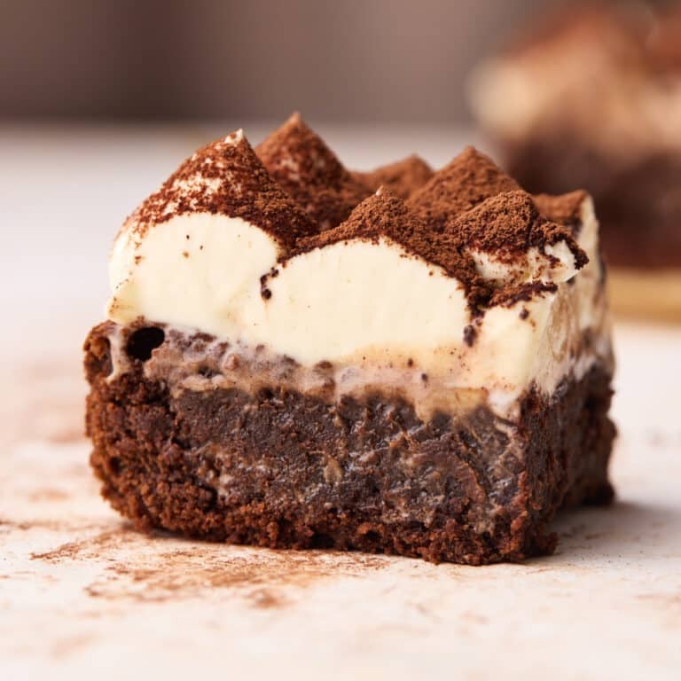 Tiramisu brownie sitting on a table showing gooey chocolate brownie with smooth mascarpone cream topping and a dusting of cocoa powder on top.