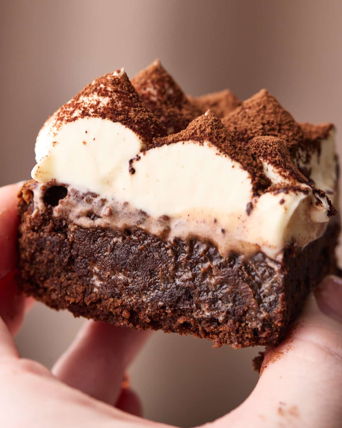 A tiramisu brownie being held up showing off the gooey chocolate brownie and smooth mascarpone cream. 