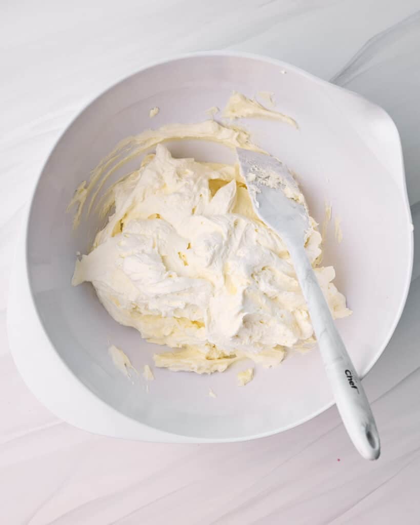 Whipped cream and mascarpone mixture being folded together in a large bowl with a spatula. 
