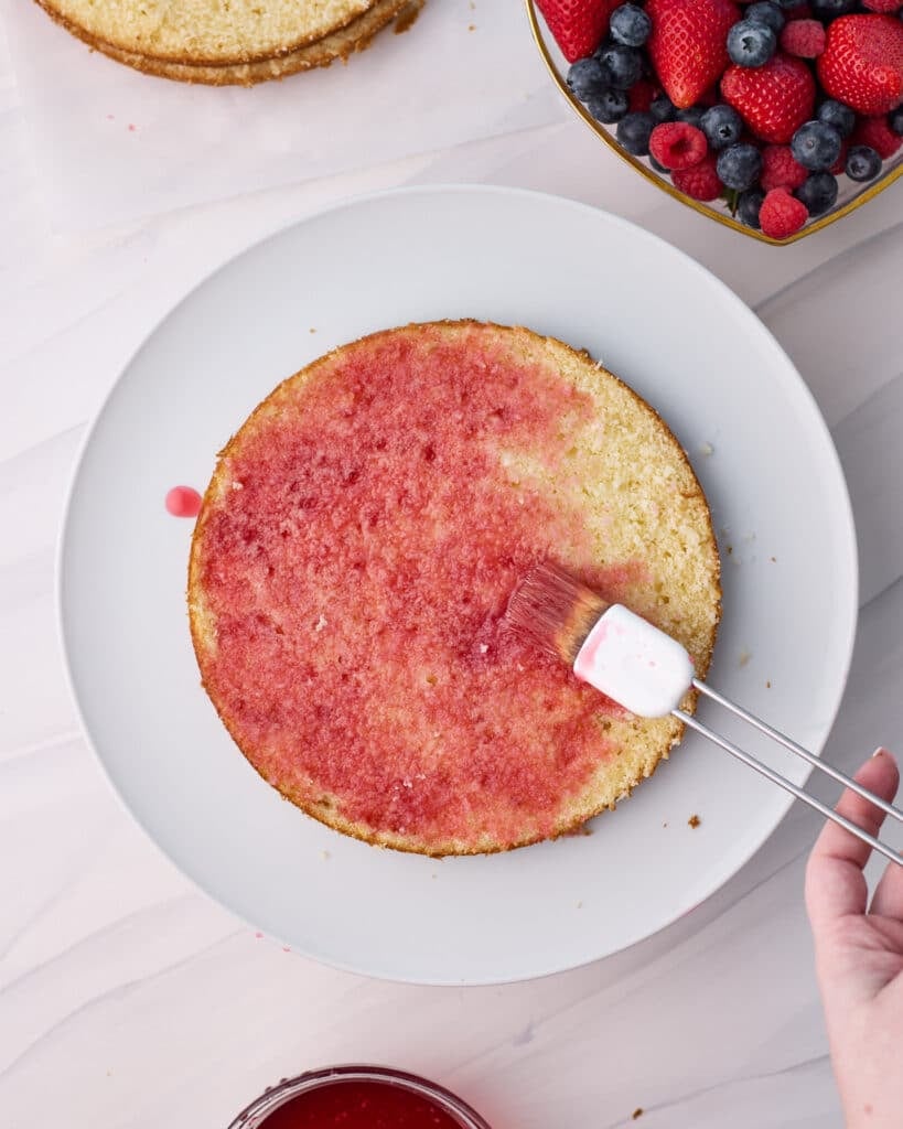 Sponge on a plate getting brushed with strawberry simple syrup.