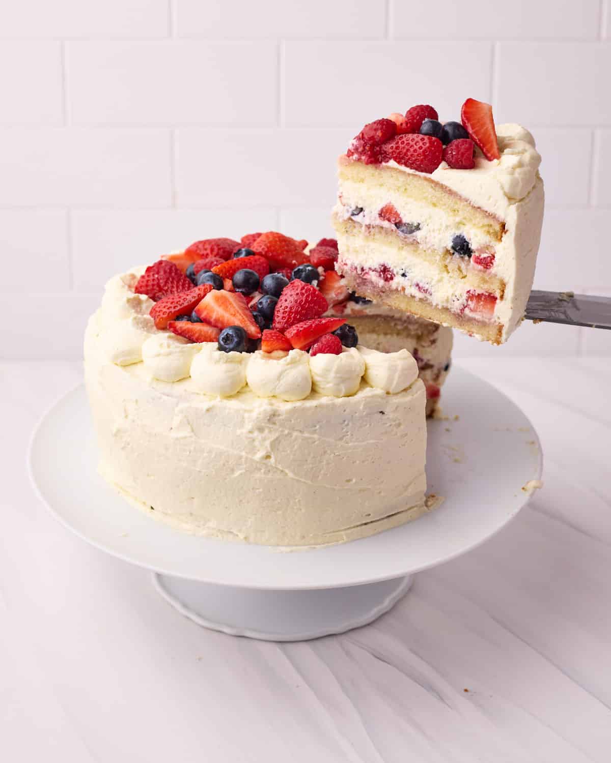 Berry Chantilly Cake on a cake stand, with a slice being cut out.