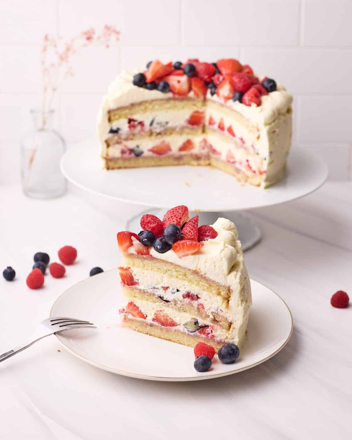 Slice of Berry Chantilly Cake on a plate, with full cake in the background. 