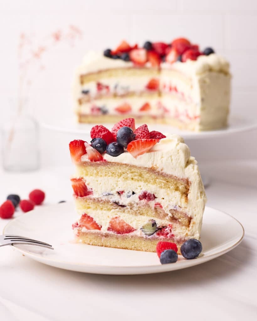 Slice of berry chantilly cake on a plate showing the chantilly cream and fresh berries in the layers inside.