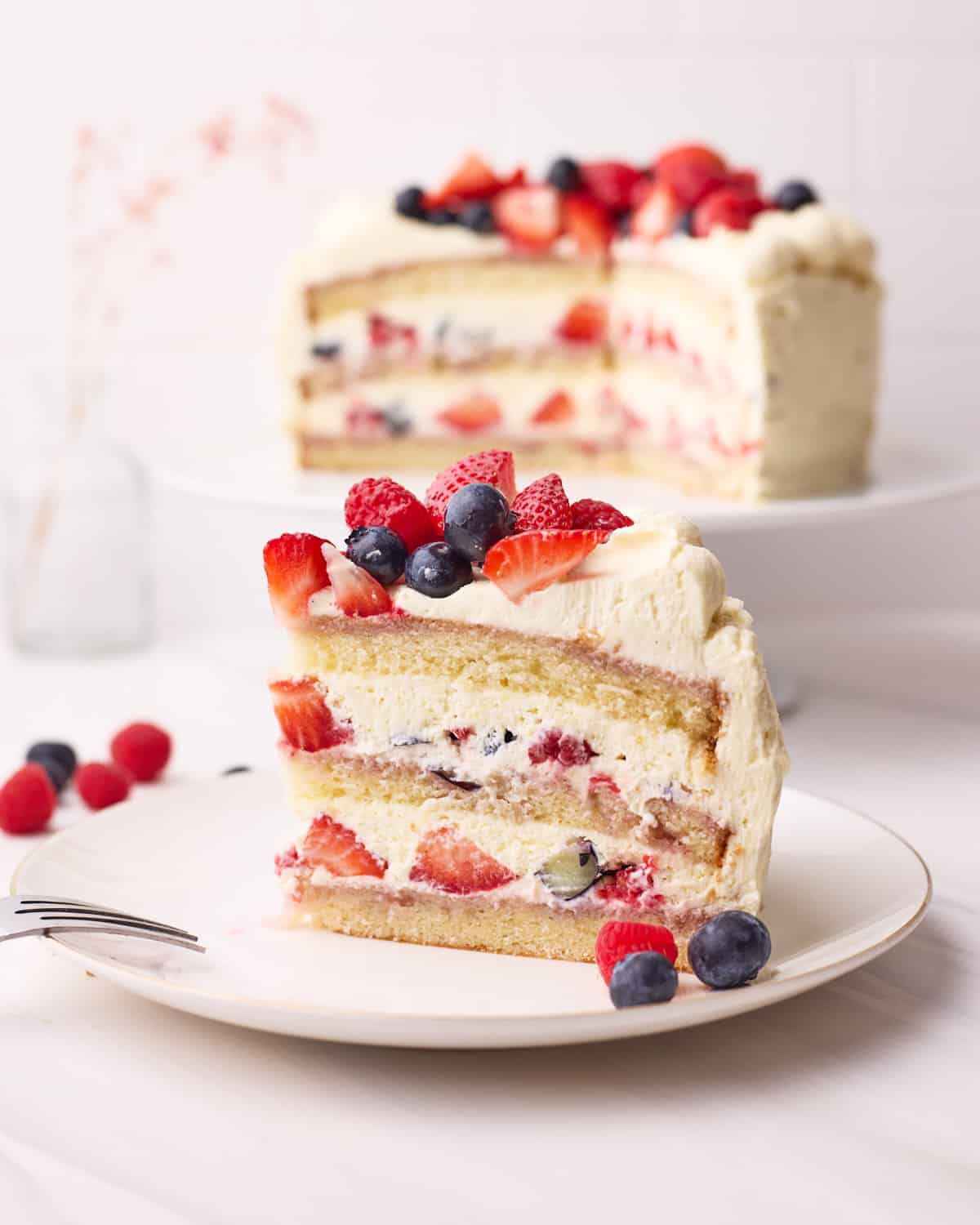 A slice of Berry Chantilly Cake on a plate, with the cake in the background.
