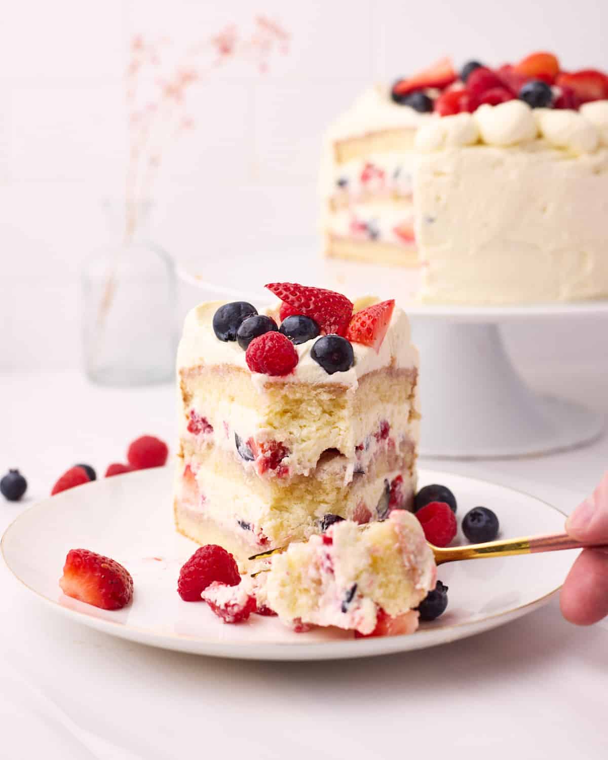 A slice of Berry Chantilly Cake on a plate, with a bit being cut out on a fork.