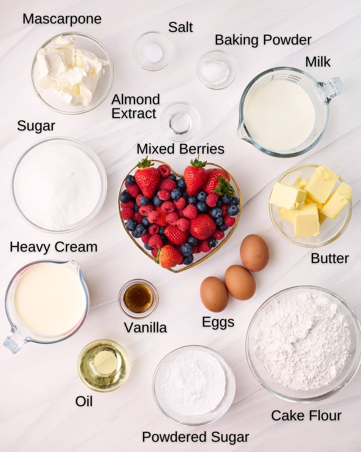 Ingredients for Berry Chantilly Cake in bowls with labels, including  mascarpone, salt, baking powder, milk, almond extract, sugar, mixed berries, butter, heavy cream, vanilla, eggs, oil, powdered sugar, and cake flour. 