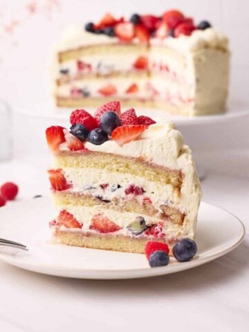 Side view of a slice of berry chantilly cake, showing the layers of fresh berries and chantilly cream inside.