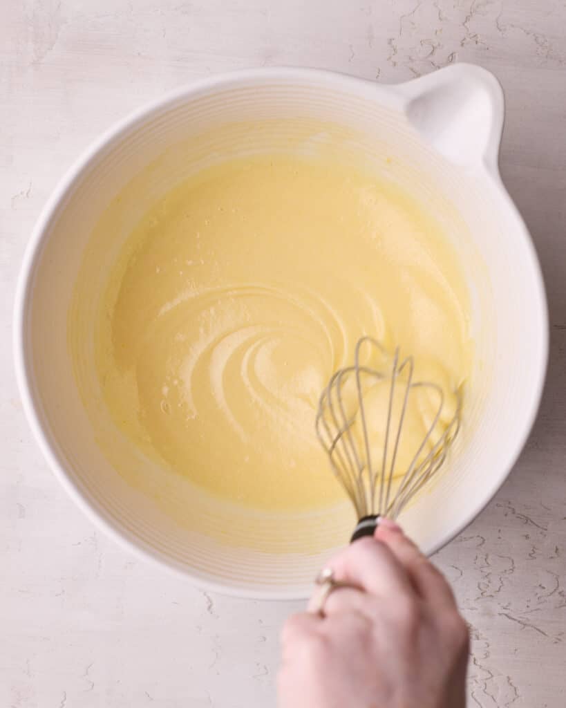 Eggs and sugar being hand whisked in a large bowl, until mixture is pale and thick.