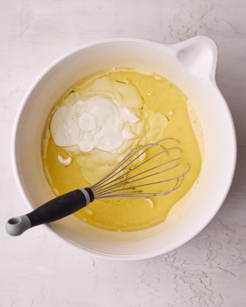 Sour cream, vanilla, and oil added into the egg mixture, ready to be whisked in a large bowl.