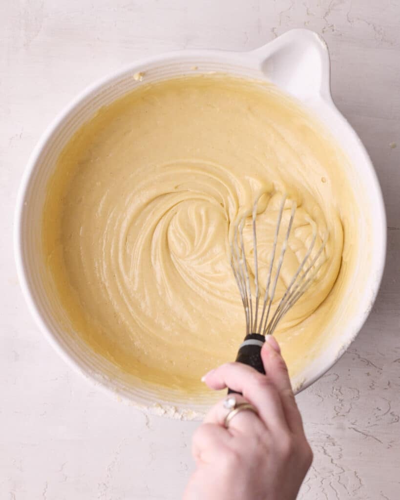 Dry ingredients being whisked into the muffin batter in a large bowl, to create a smooth and lump free mixture.