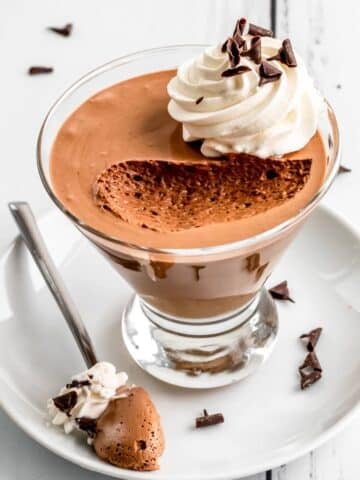 Chocolate mousse in a glass with whipped cream on top and a spoonful taken out to show the silky texture.