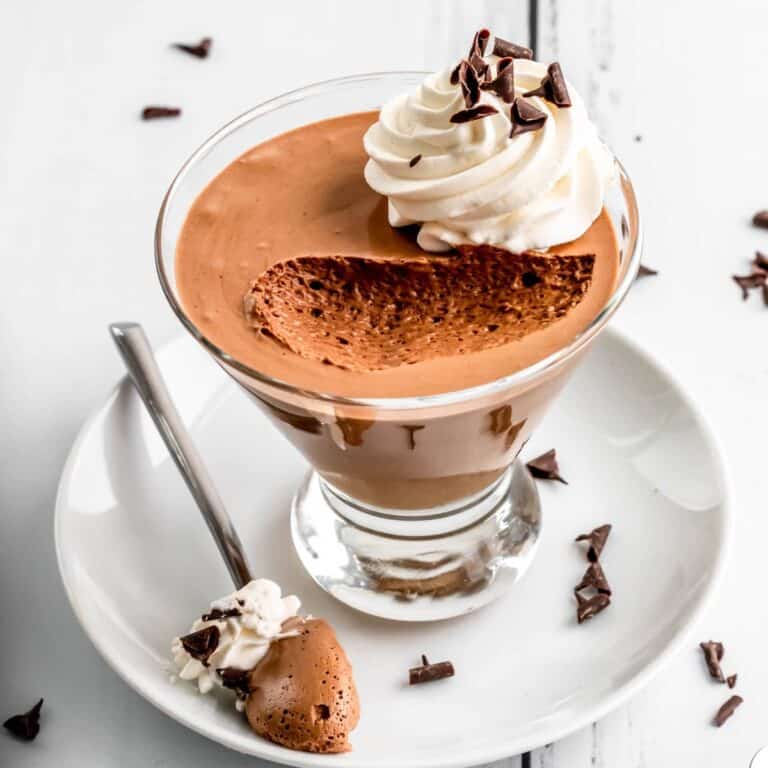 Chocolate mousse in a glass with whipped cream on top and a spoonful taken out to show the silky texture.