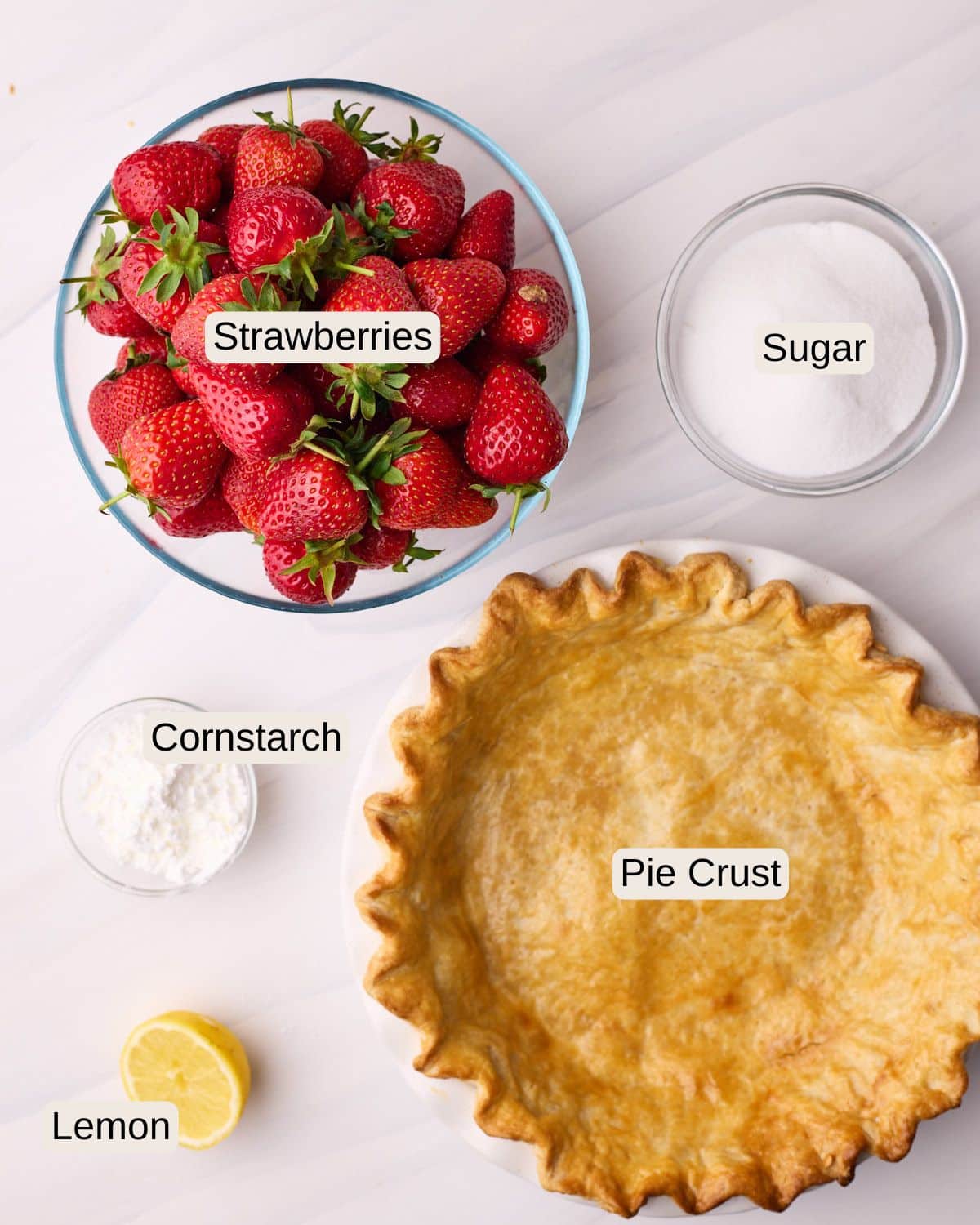 Labelled ingredients for strawberry pie, including strawberries, sugar, cornstarch, pie crust, and a lemon. 