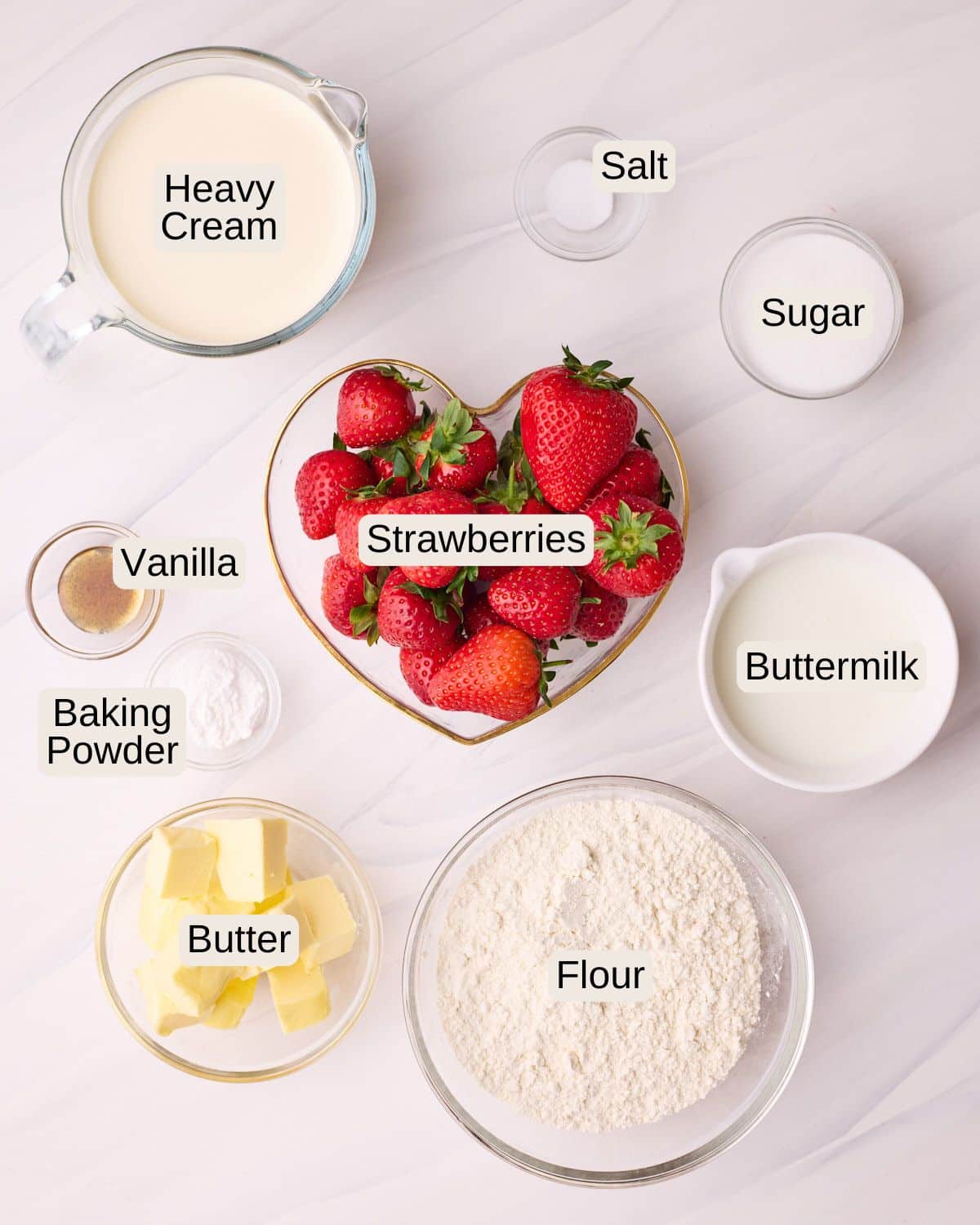 Labelled ingredients for strawberry shortcake, including heavy cream, salt, vanilla, strawberries, sugar, buttermilk, baking powder, butter, and flour.