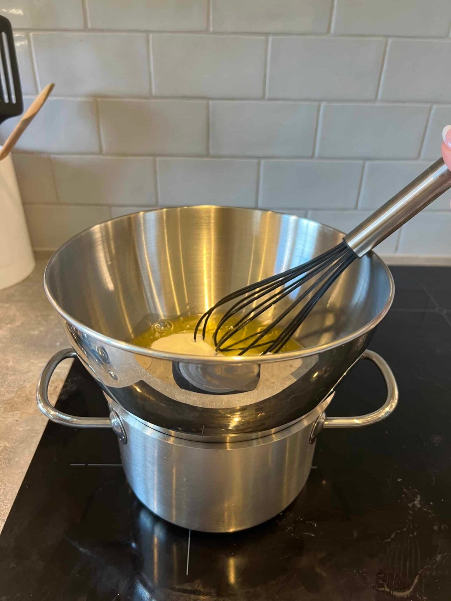 Double boiler with egg whites, sugar, and cream of tartar in the bowl over the saucepan.