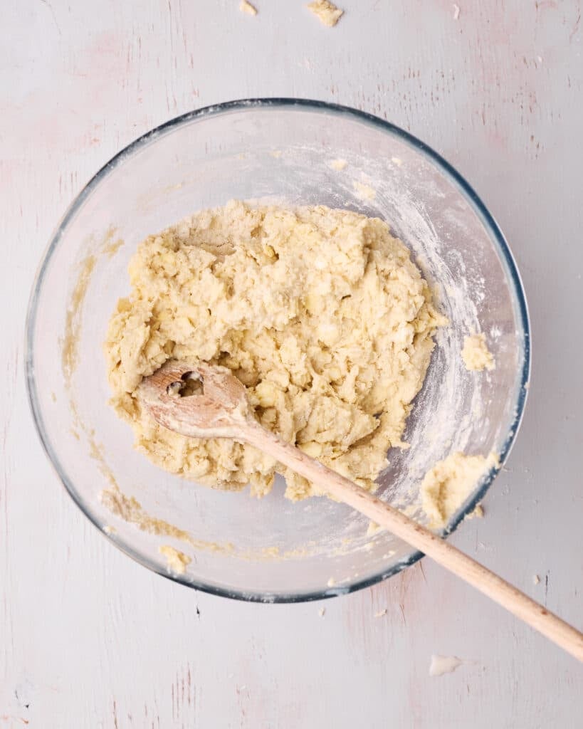 Wet ingredients mixed into the flour mixture with a wooden spoon to create a shaggy dough.