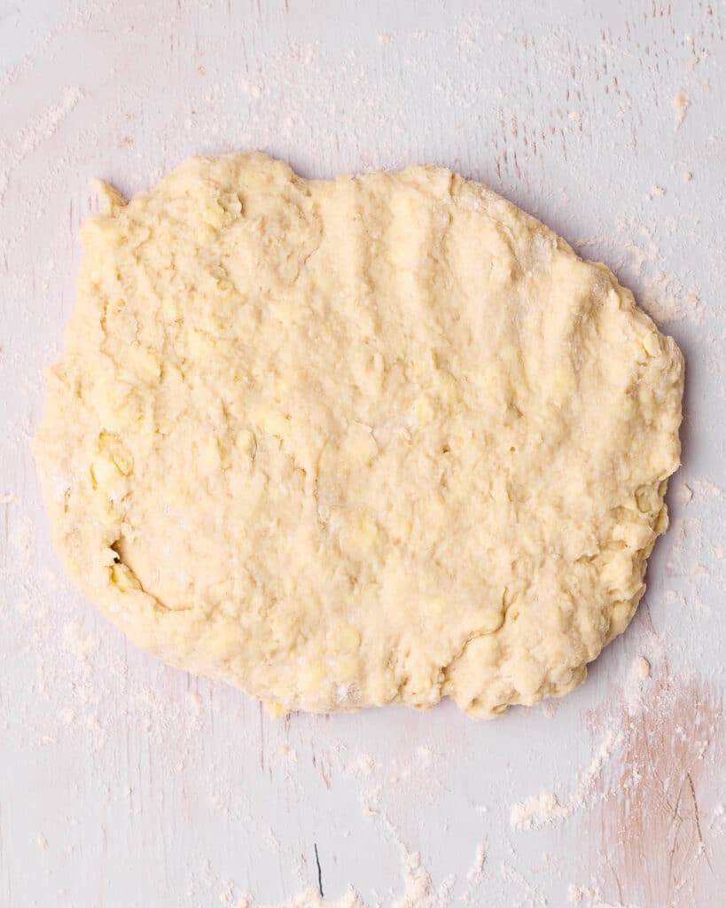 Scone dough flatten out onto a floured surface, shaped into a rough rectangle.