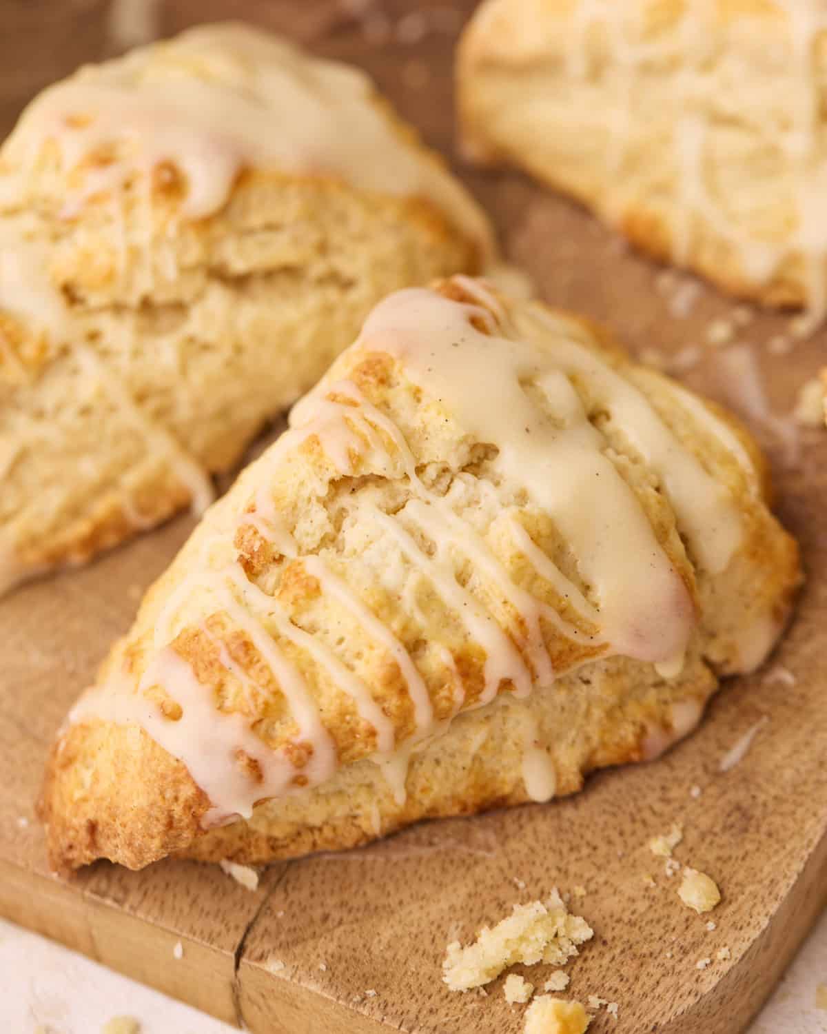 Scone drizzled with a glaze, sitting on a wooden board.