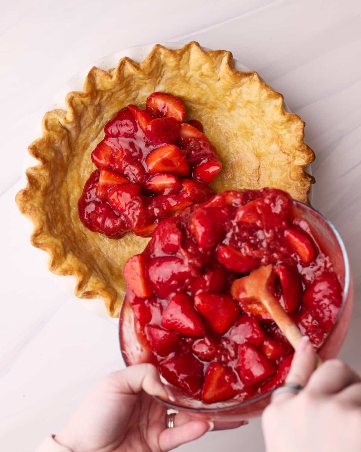Strawberry pie filling being poured into the pie crust.