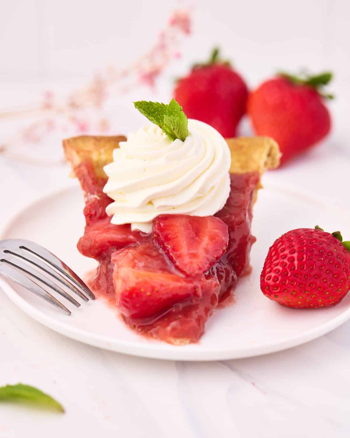 Slice of strawberry pie on a plate with a dollop of chantilly cream on top.