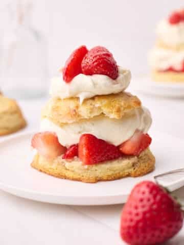 Finished strawberry shortcake on a plate with a fork beside it.