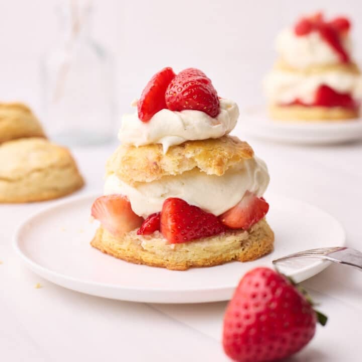 Finished strawberry shortcake on a plate with a fork beside it.