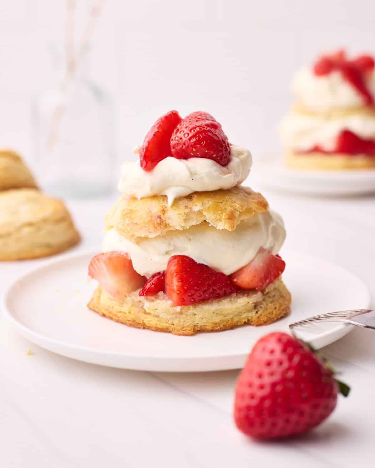 Finished strawberry shortcake on a plate with a fork beside it.